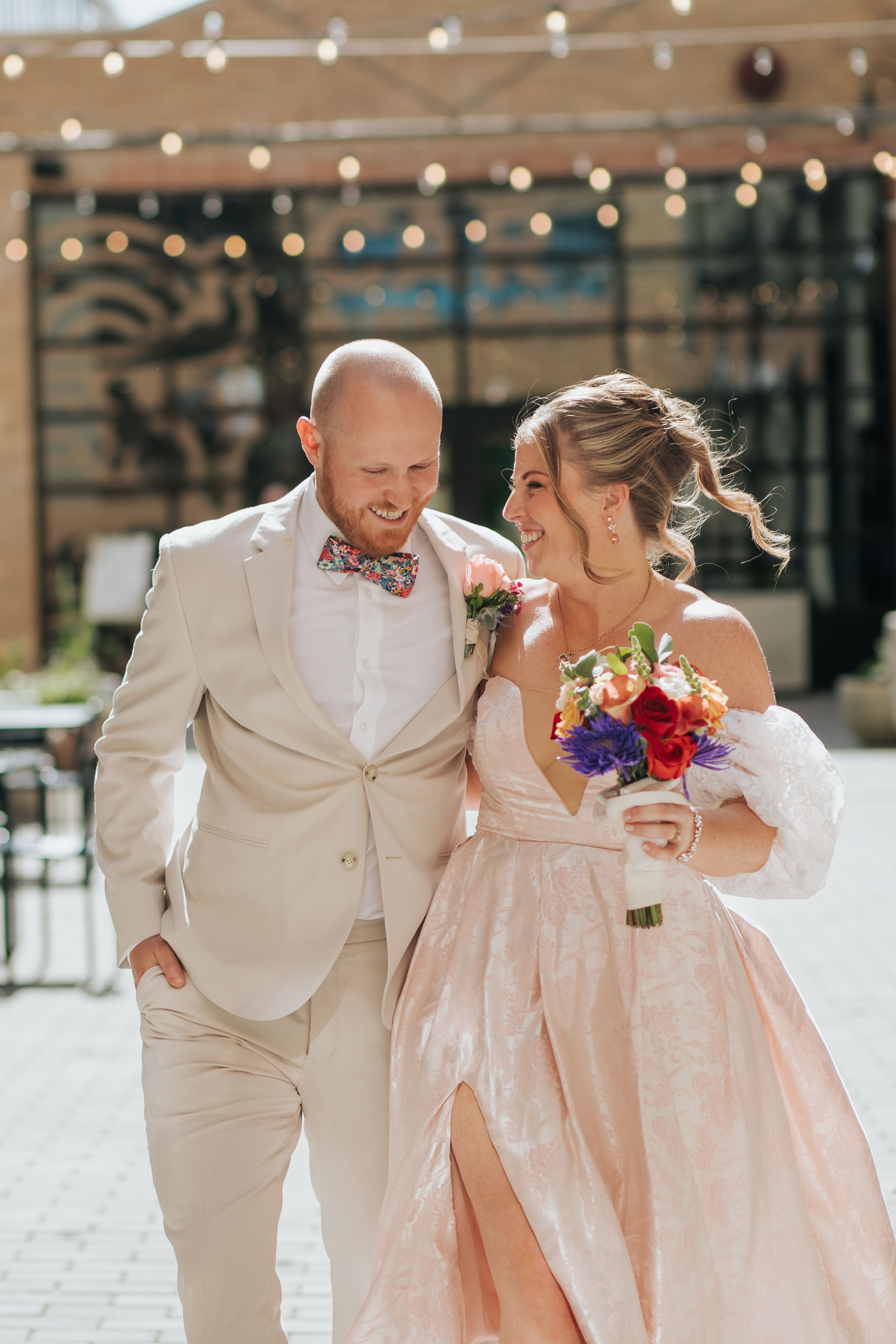 Joyful wedding couple in white and blush pink outfits share a candid laughing moment together outdoors.