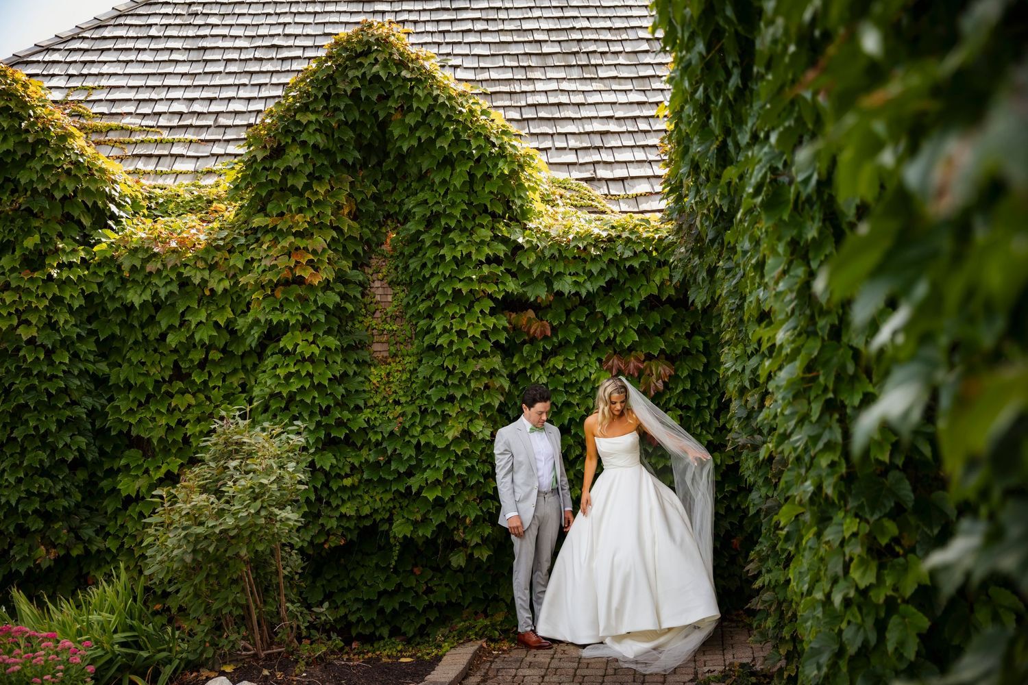 Wedding couple poses under ivy-covered walls during golden hour.
