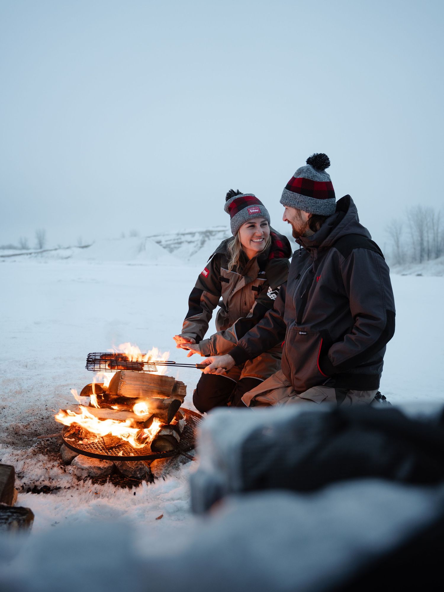 Friends enjoying conversation around warm campfire while ice fishing at dusk.