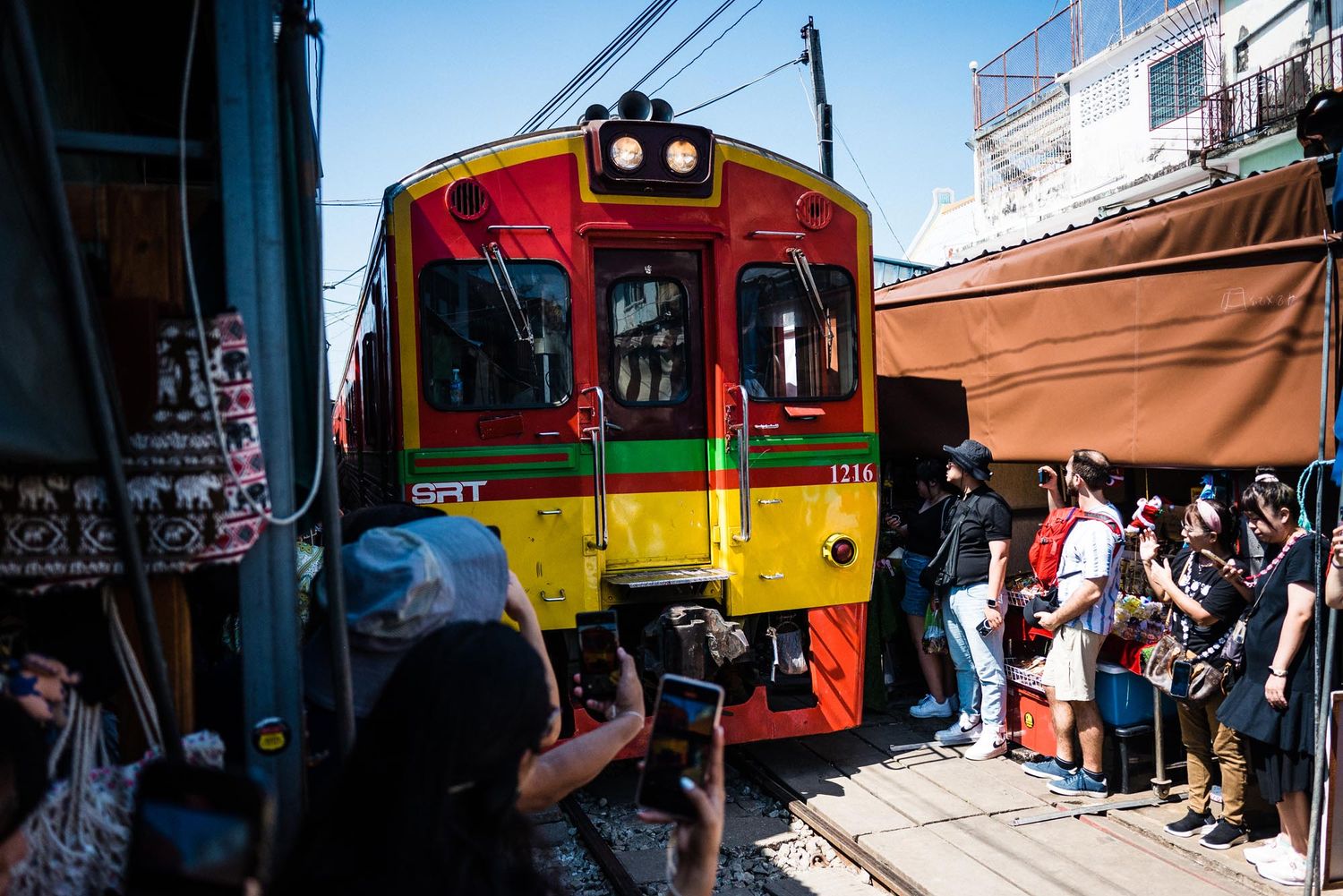 Tourists gather to photograph a colorful red and yellow train at the Maeklong Railway Market in Thailand.