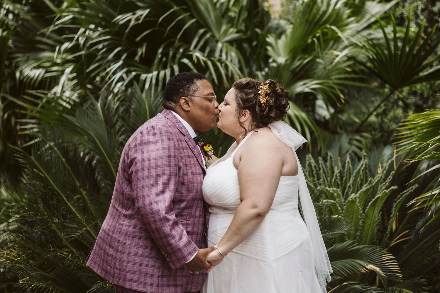 A couple shares romantic moments in a lush tropical garden setting wearing wedding attire.