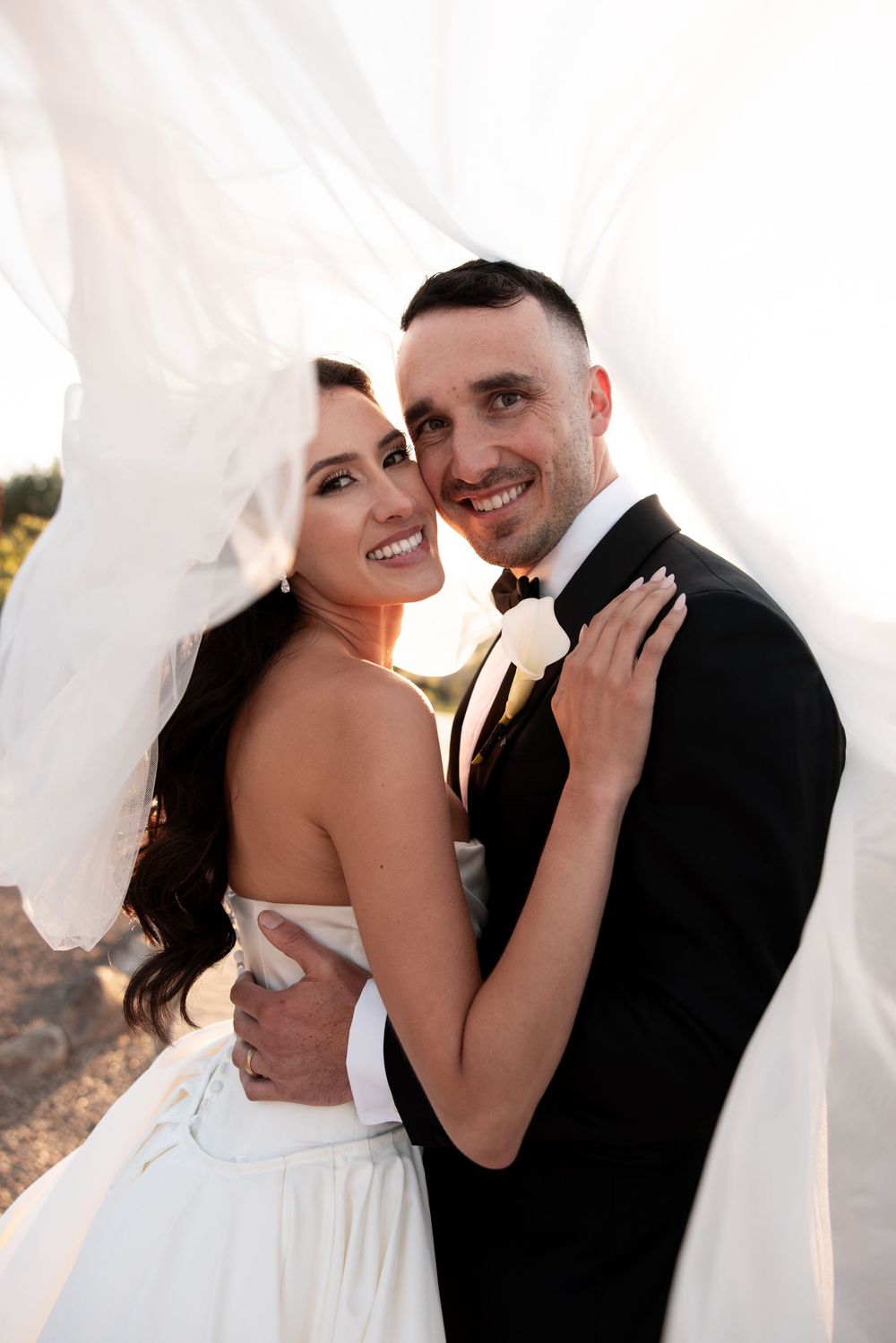 A romantic wedding photo series showing a couple embracing under a flowing white veil in natural outdoor lighting.