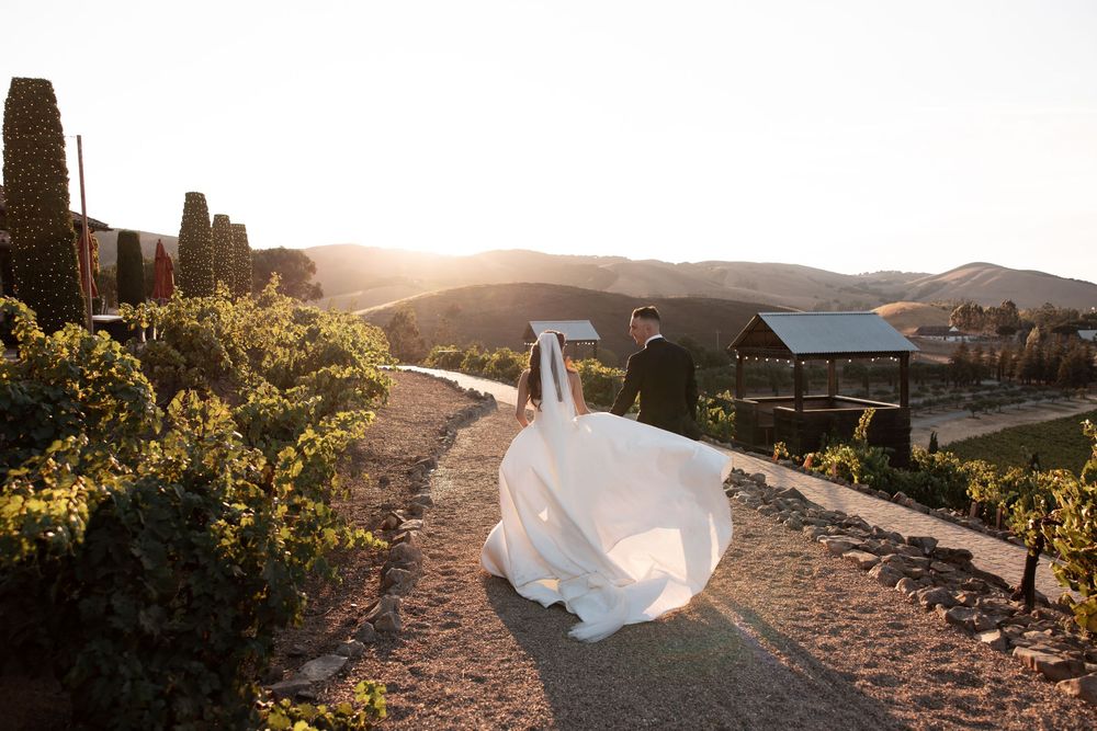 A bride's white wedding dress train flows gracefully in the wind against a scenic mountain landscape at sunset.