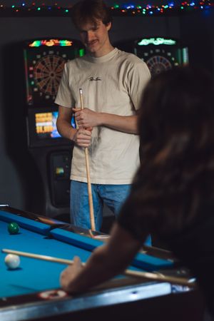 Young man smiling with a pool cue while his partner takes a shot at a blue billiard table during photoshoot at tommys tavern in yelm wa