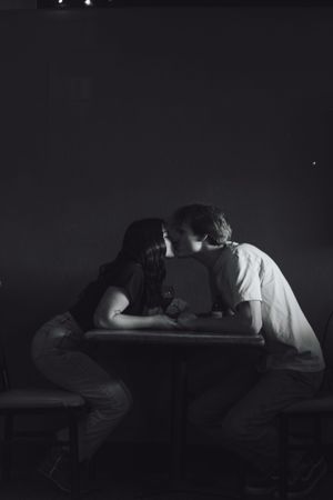 Black and white photo of a couple sharing a kiss across a wooden table in a dark, intimate setting at a dive bar in yelm washington