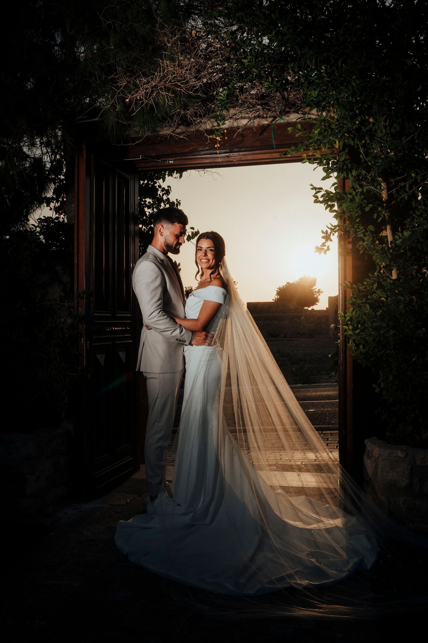A romantic wedding moment captured among lush greenery with two people embracing in formal attire.