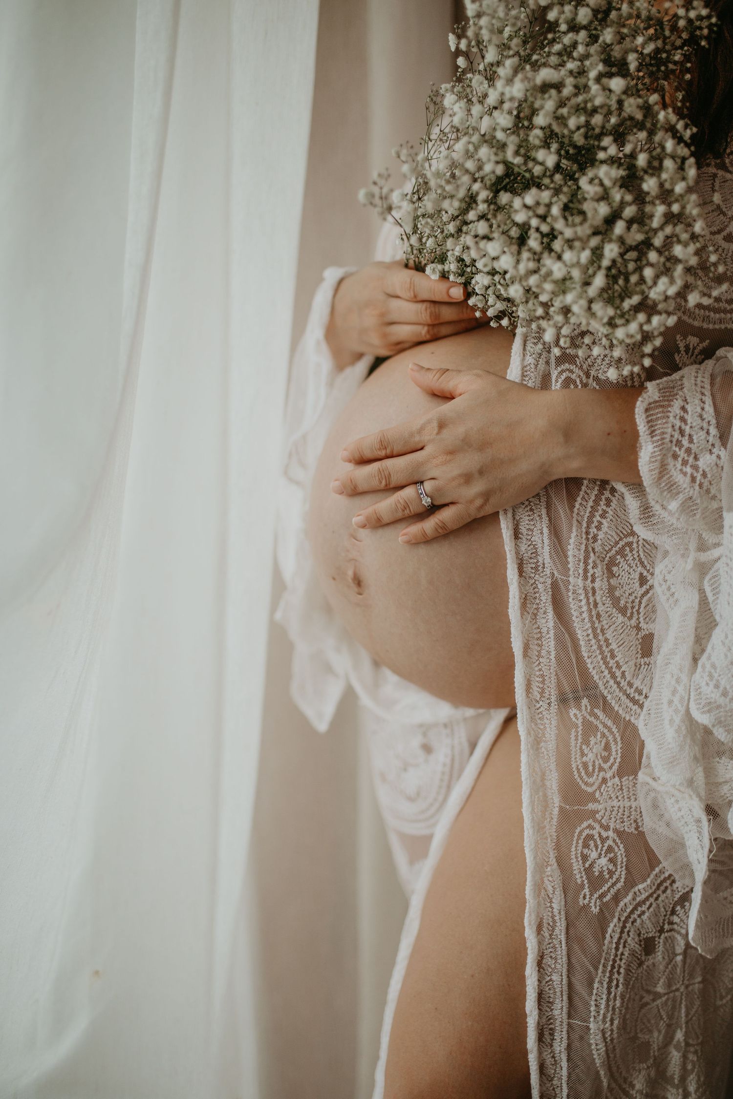Delicate white lace wedding dress details shown in soft natural light with baby's breath flowers.