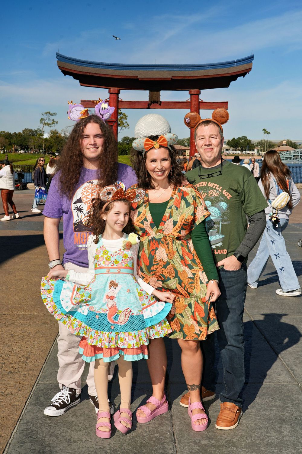 A group wearing colorful Disney-themed outfits and Mickey ears poses together at a theme park.