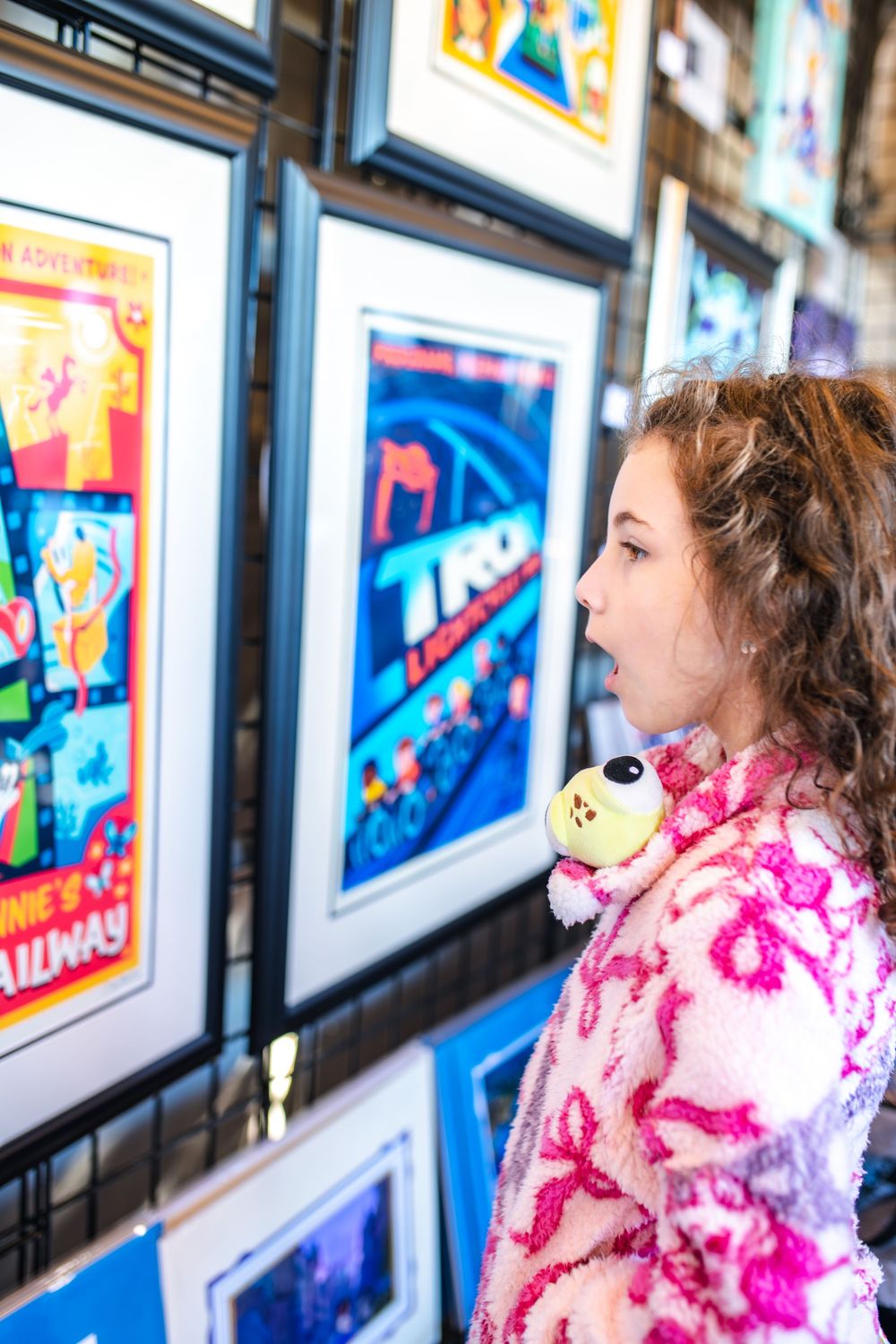 Young visitor admires colorful artwork displayed in gallery with bright framed pieces along wall.