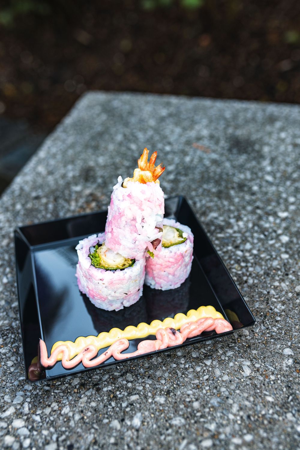 Close-up sequence of colorful sushi rolls with pink rice and toppings being arranged on a black serving plate.