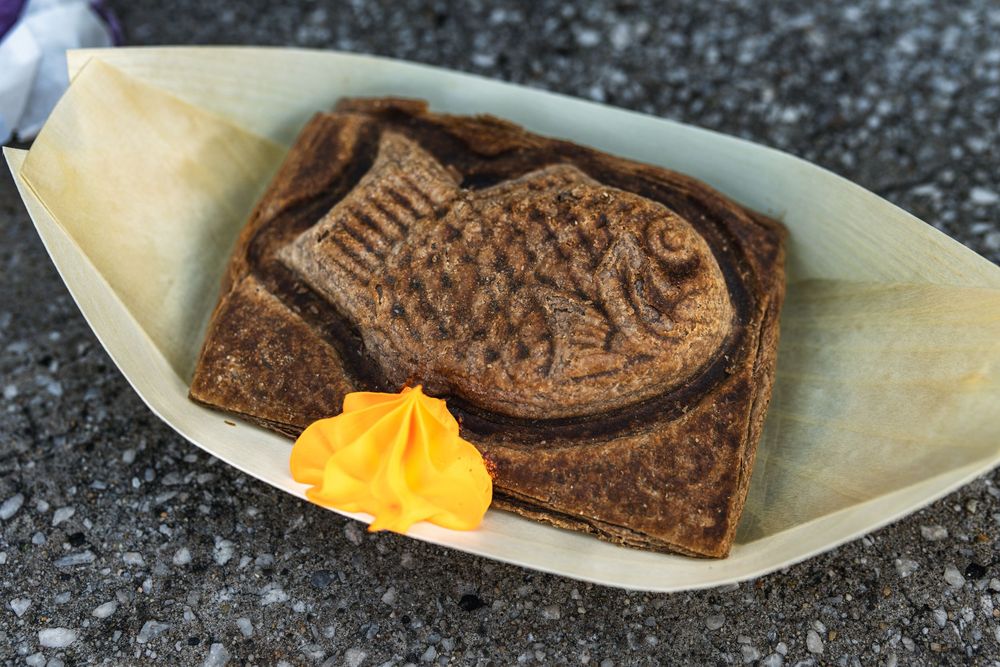 Chocolate fish-shaped taiyaki pastries filled with orange cheese being prepared on wooden plates.