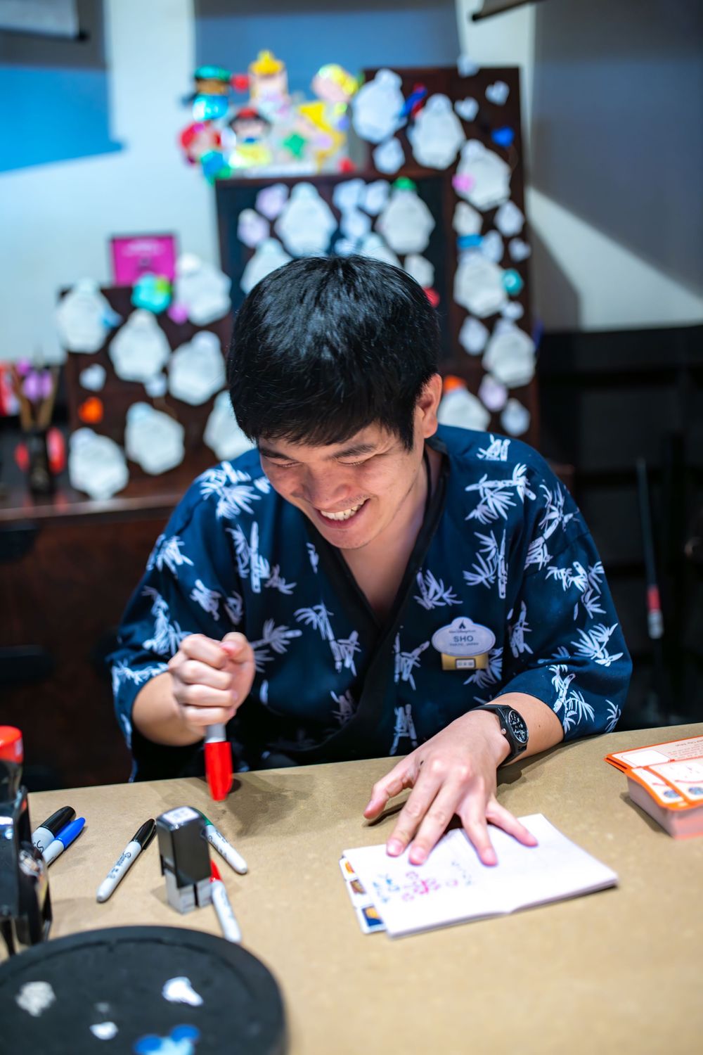 A person wearing a blue patterned shirt writes or draws on paper in a sequence of progressive shots.