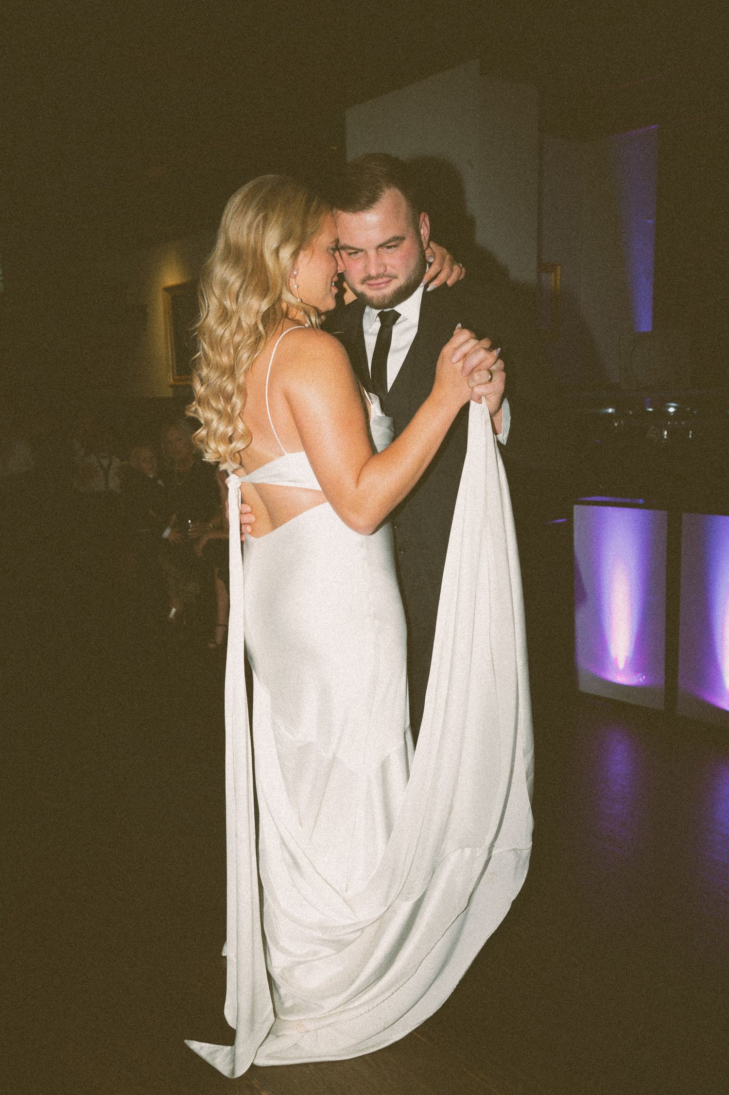 A couple dances together at a wedding reception with purple uplighting visible in the background.