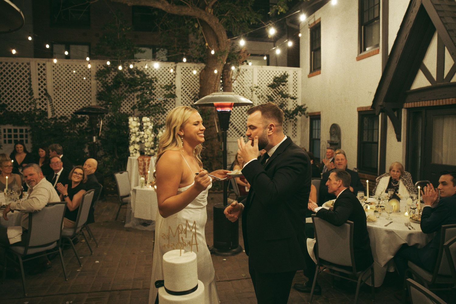 Wedding reception guests enjoy dinner and dancing under string lights in an intimate indoor venue setting.