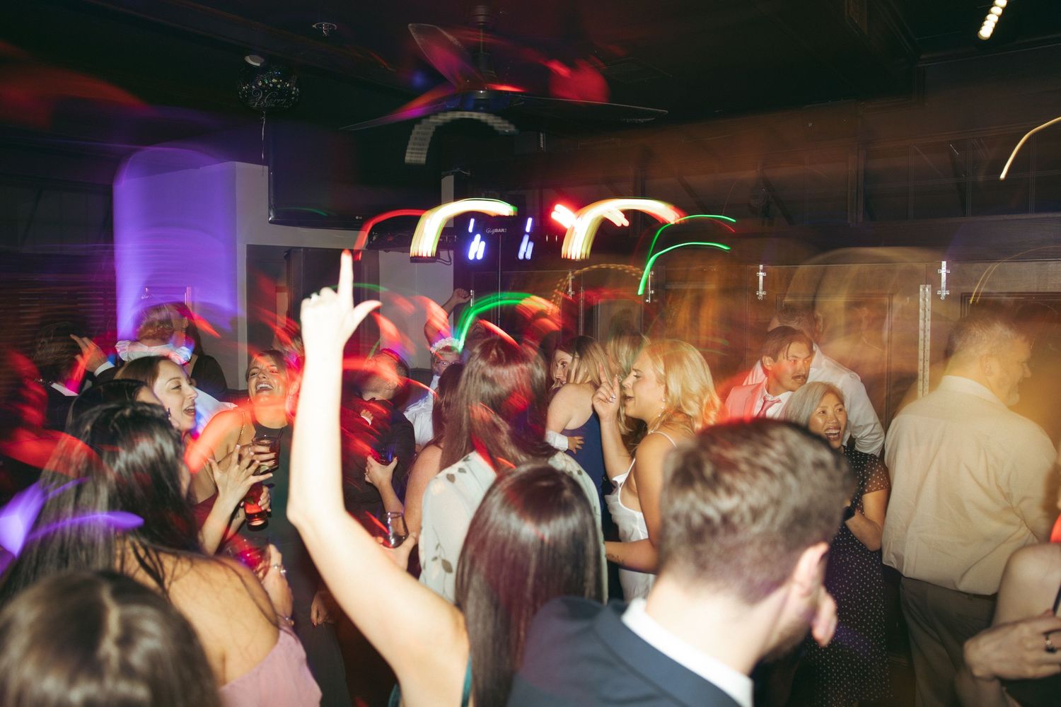Crowded nightclub dance floor with colorful purple and red lighting effects creating an energetic party atmosphere.