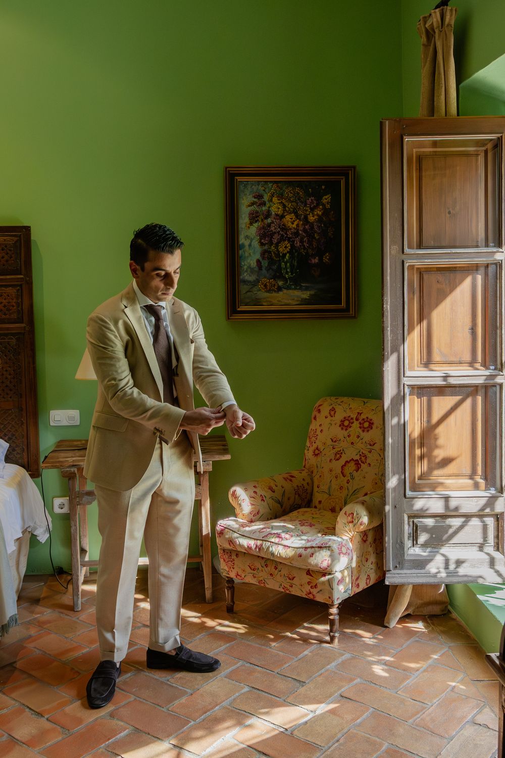 A sequence showing someone in a beige suit getting ready in a room with green walls and terracotta floors.