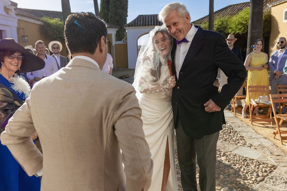 A couple shares a joyful moment at their outdoor wedding ceremony with guests looking on in the sunlight.