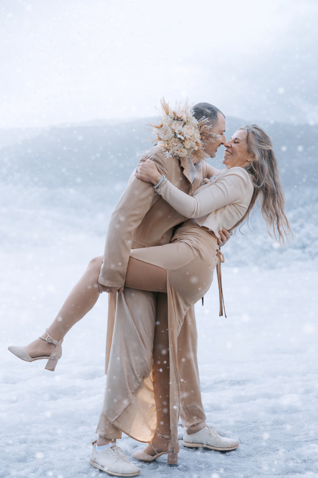 Person in beige winter coat plays joyfully with small dog in snowy winter landscape during golden hour lighting.