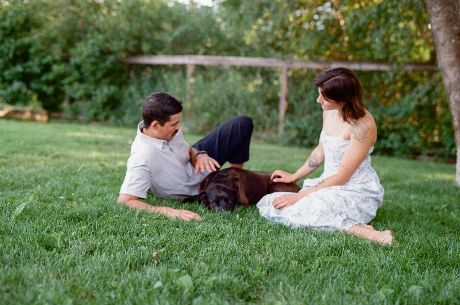 35 mm film photo of a husband and wife laying in the grass with their dog