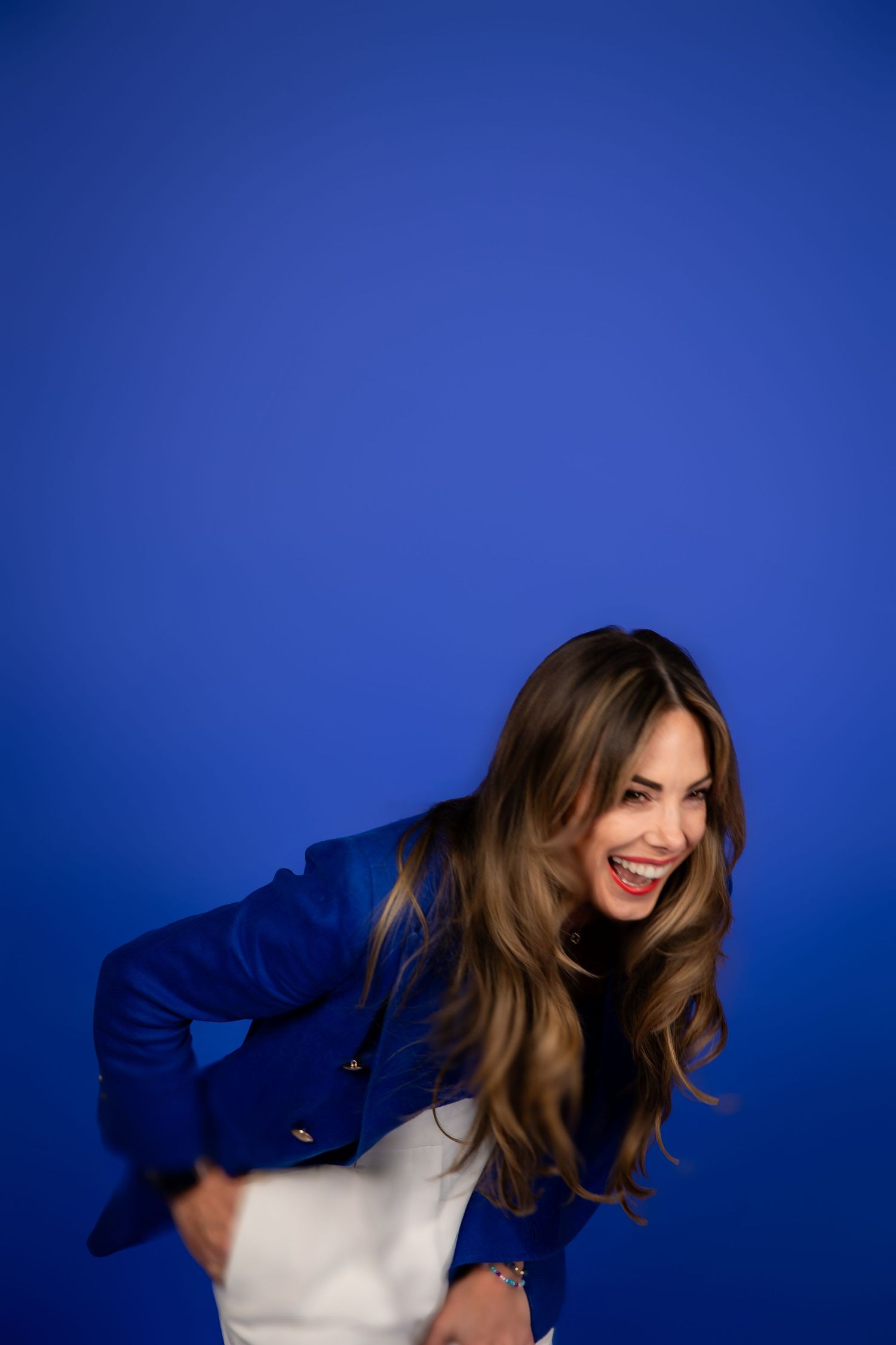 Person in white top against vibrant blue background laughs and leans forward with dynamic movement.