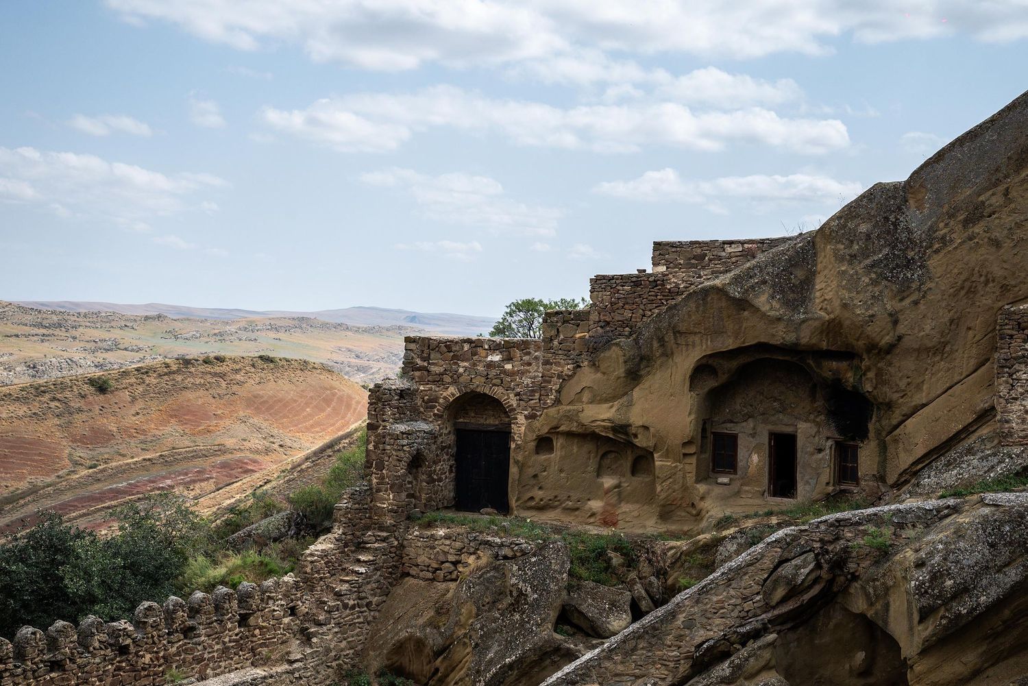 Ancient cave dwellings carved into rocky cliffs overlook a vast desert landscape under blue skies in Georgia's Vardzia.