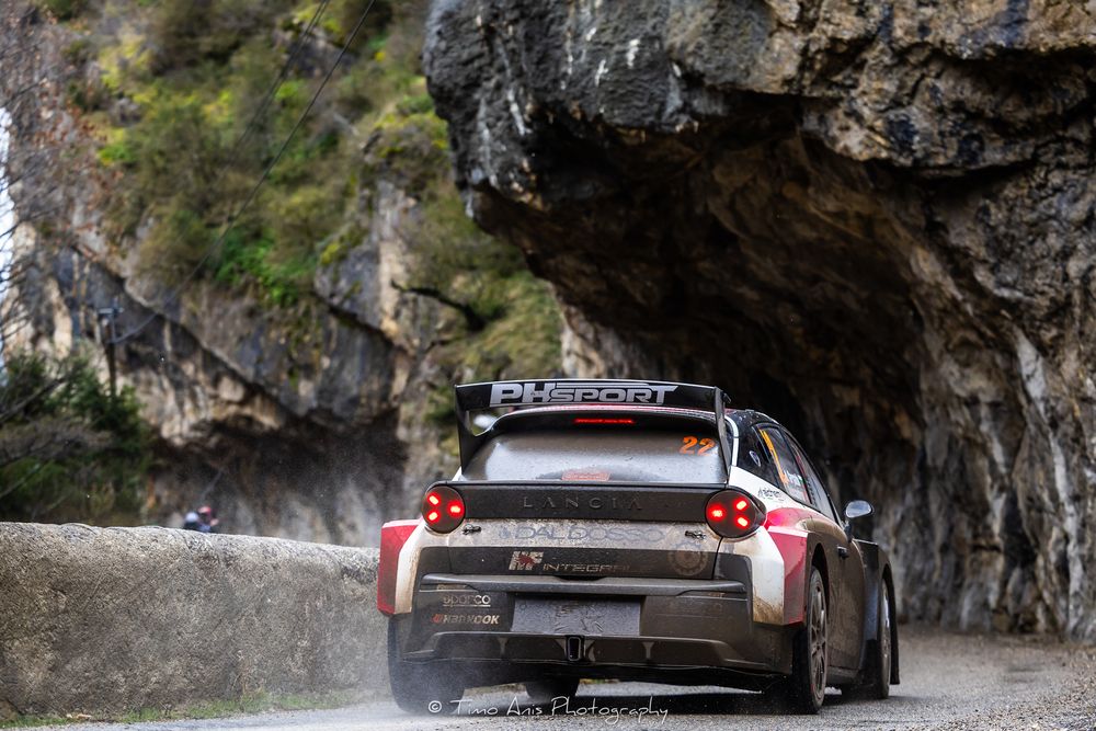 A black Porsche sports car drives along a winding mountain road with steep cliffs and rocky terrain.