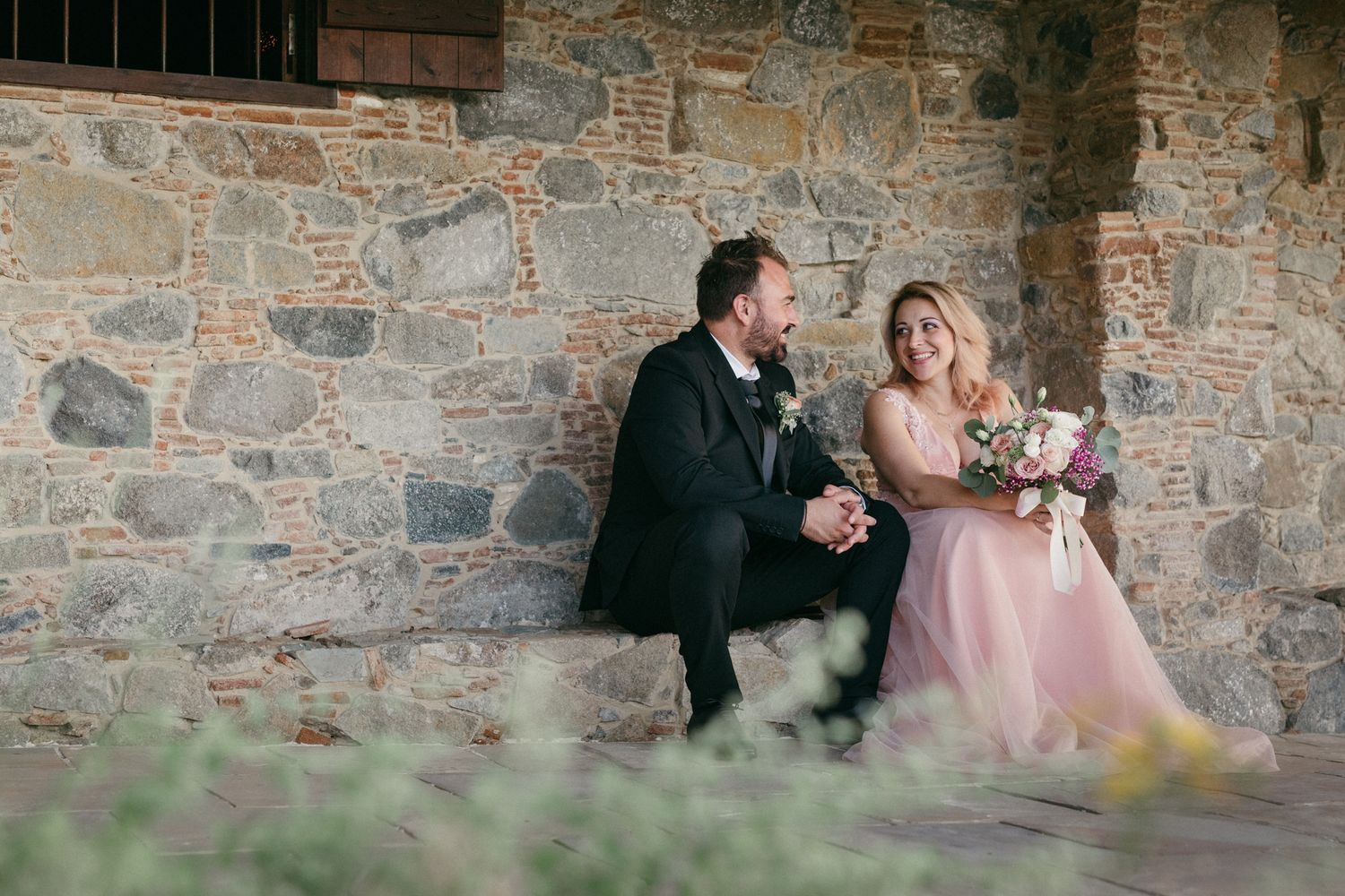 A romantic couple shares tender moments against a rustic stone wall backdrop during their wedding photoshoot.