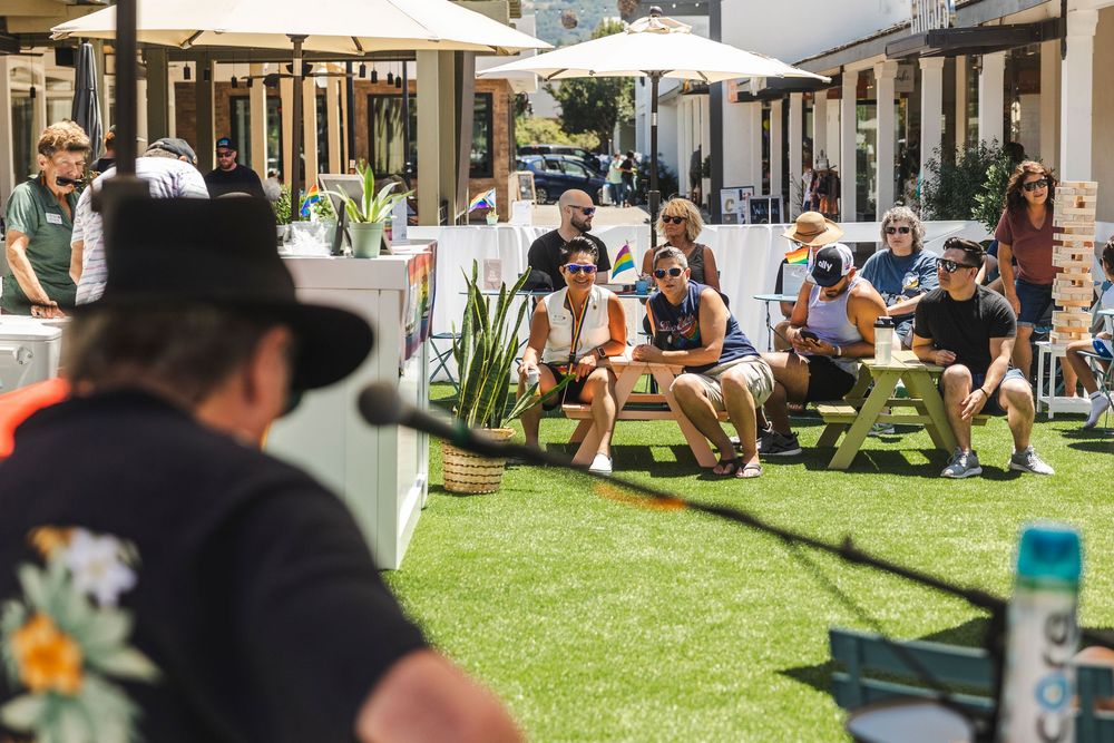 People relaxing on a grassy lawn outside a modern building with picnic tables and benches in the background.