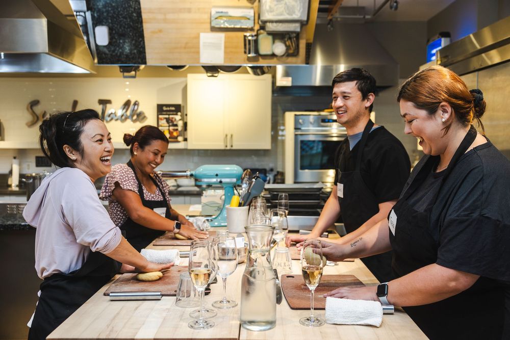 Restaurant staff members gather around a prep table during a pre-service meeting in a modern kitchen setting.