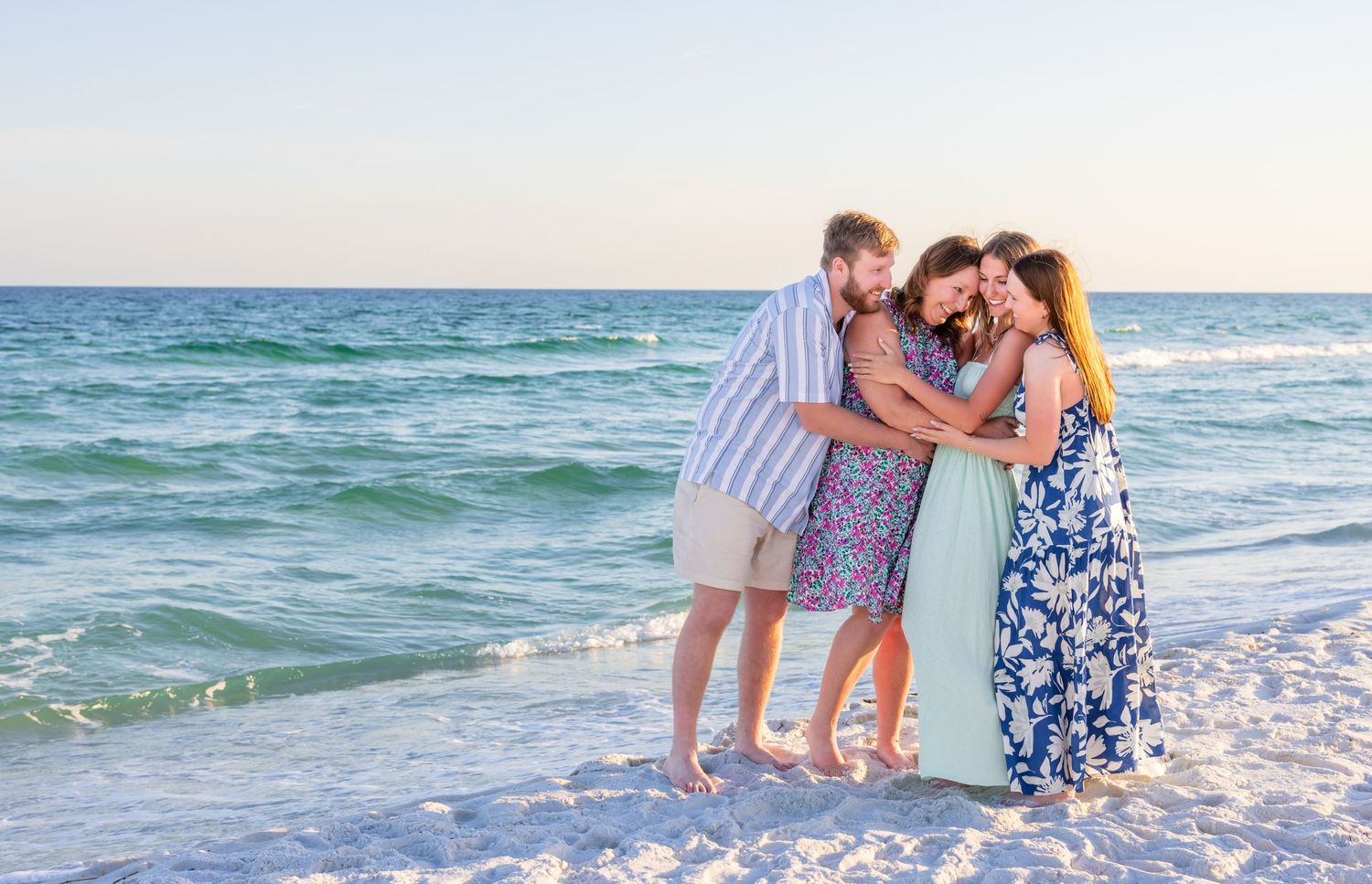 Romantic couple embraces while walking along a sandy beach at sunset with ocean waves in the background.