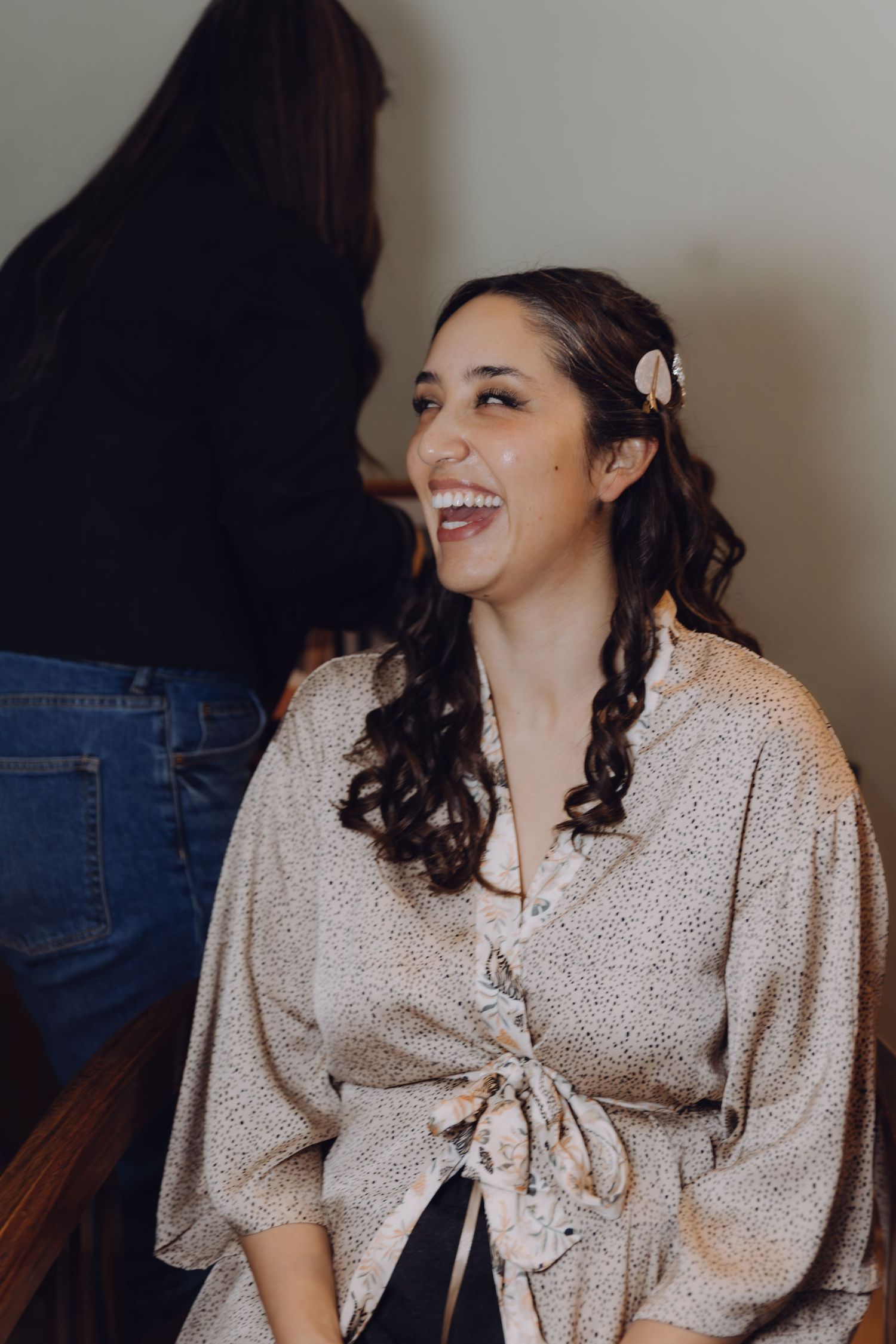 Bride laughs joyfully while getting hair and makeup done during wedding morning preparations.