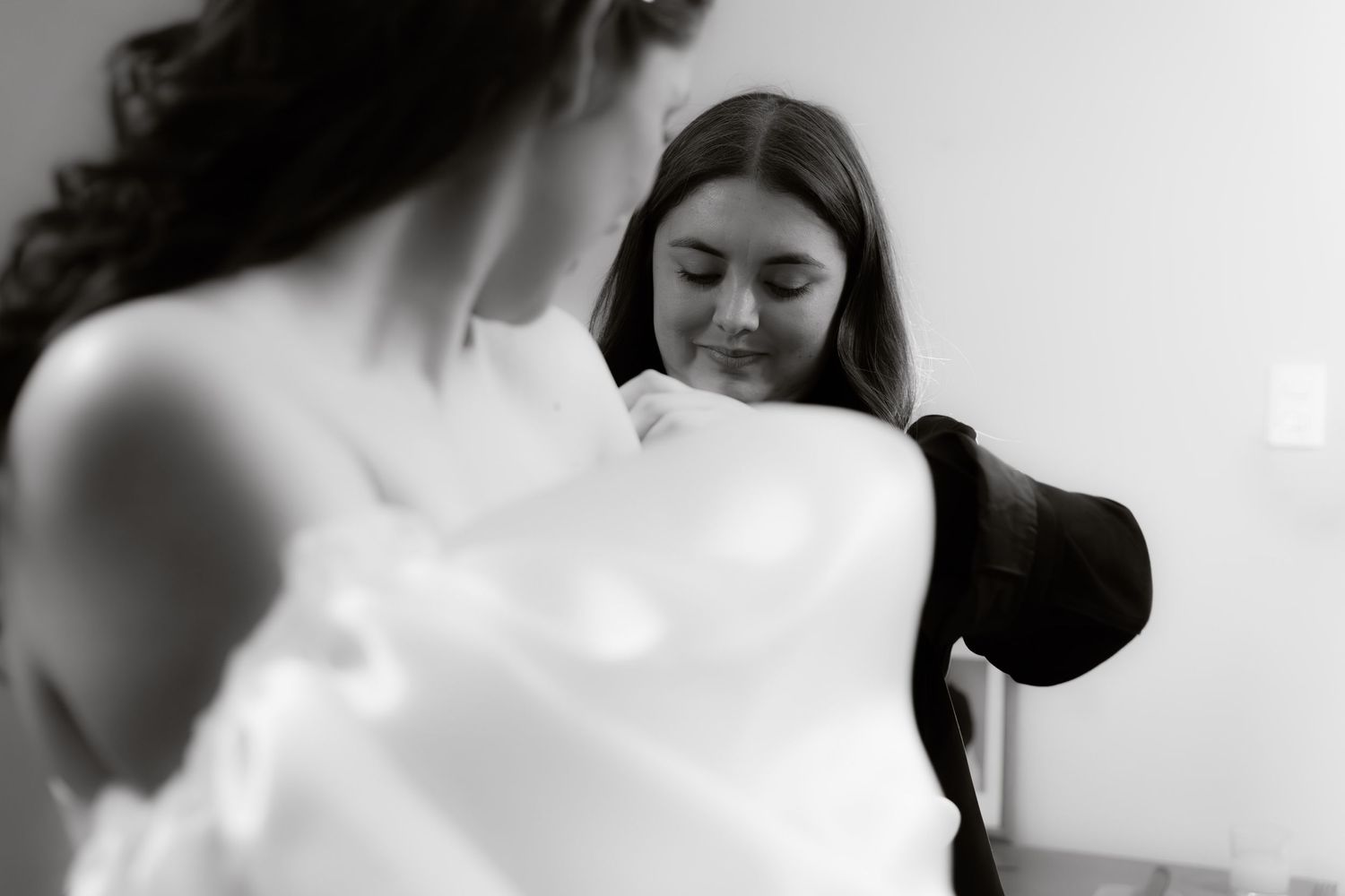 Bridesmaid helping bride with white wedding dress in black and white photo.