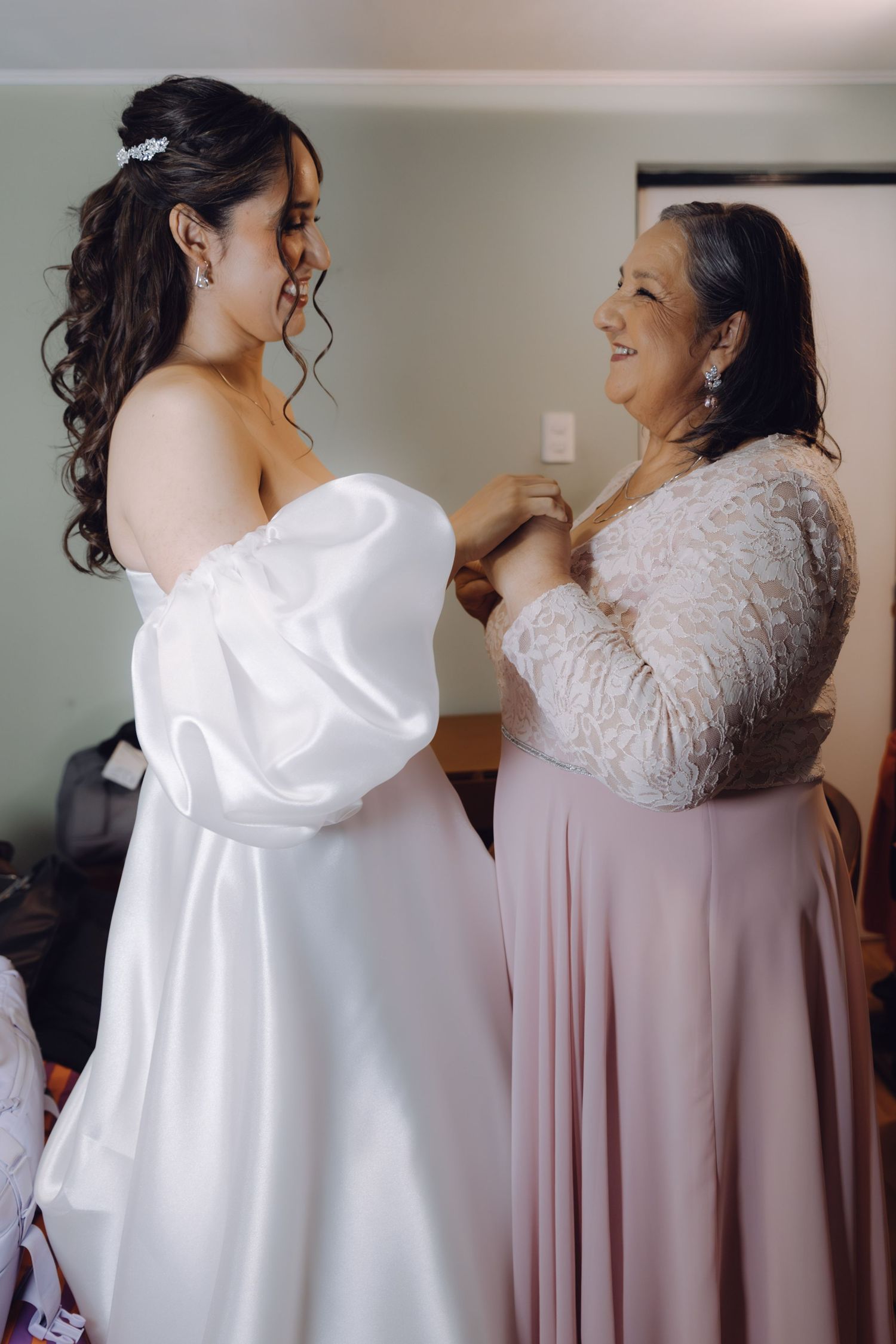 Bride in white puff sleeve gown holding hands with mother in pink dress before wedding.