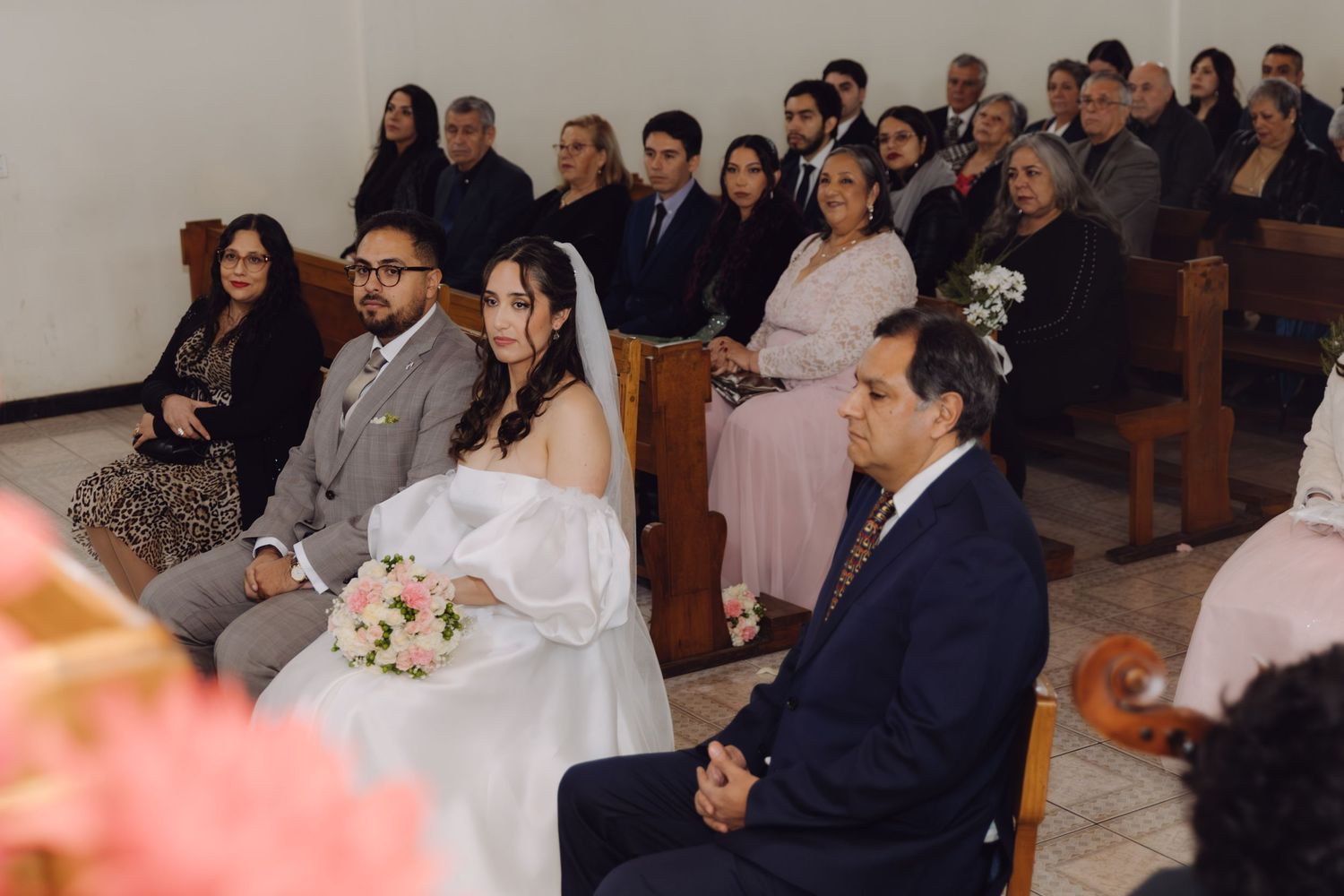 Bride and groom seated with guests during Catholic wedding ceremony in a church.