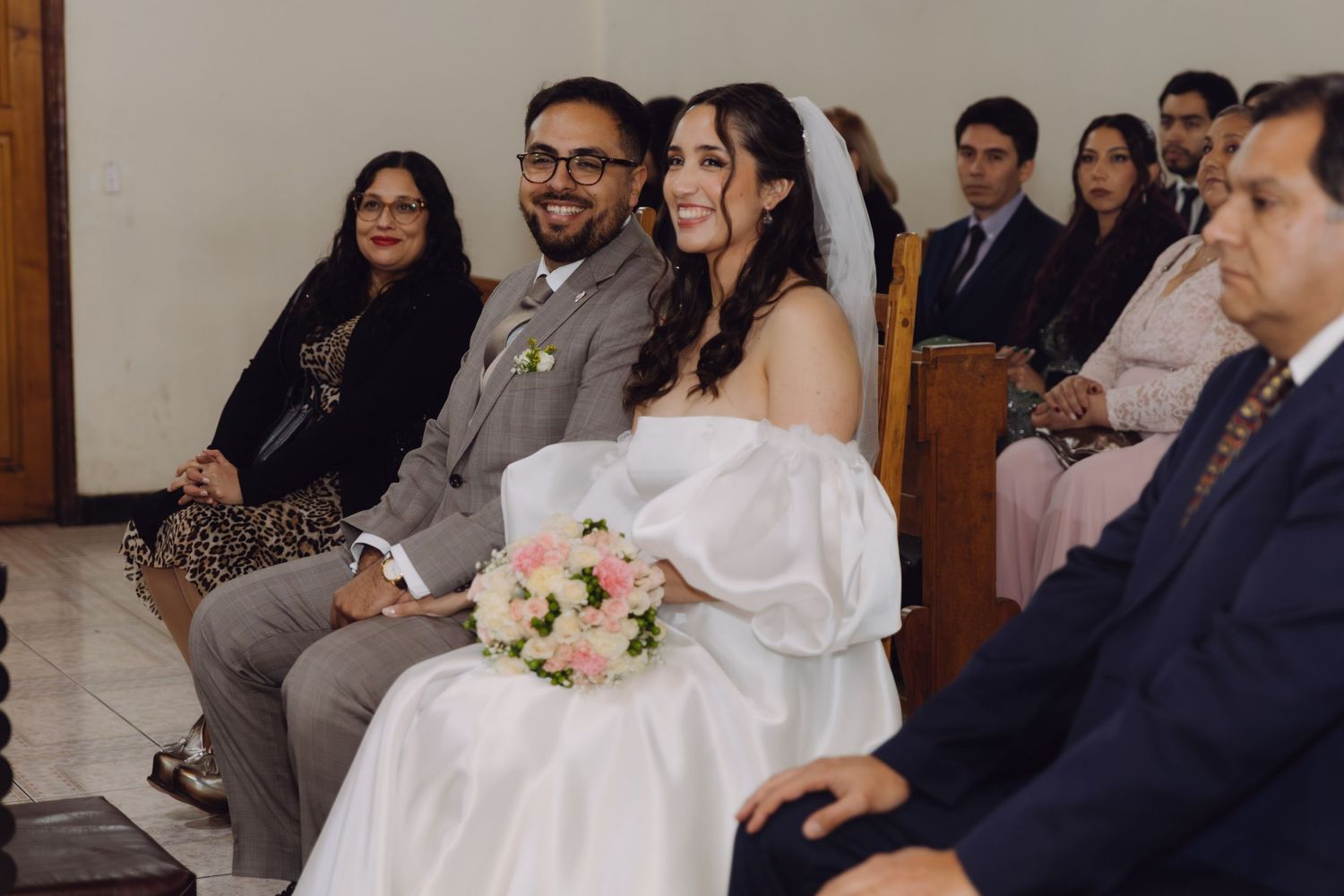 Happy bride and groom smiling while seated together during Catholic wedding ceremony.