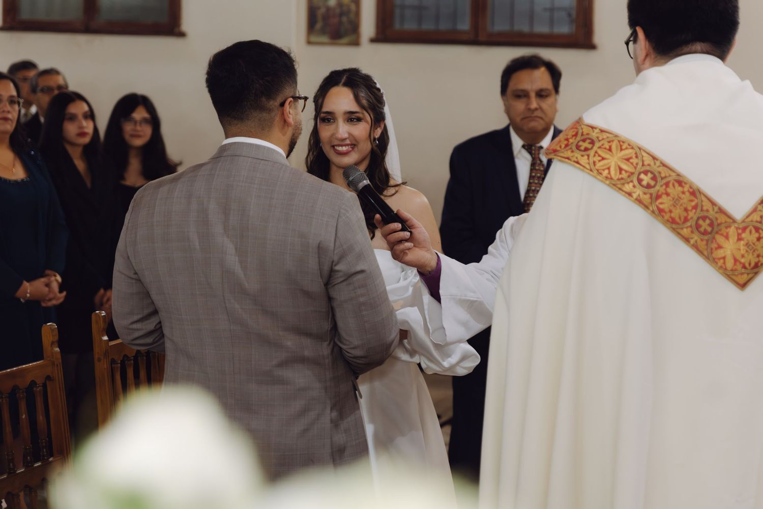 Bride smiling while priest performs wedding ceremony ritual at Catholic church altar.