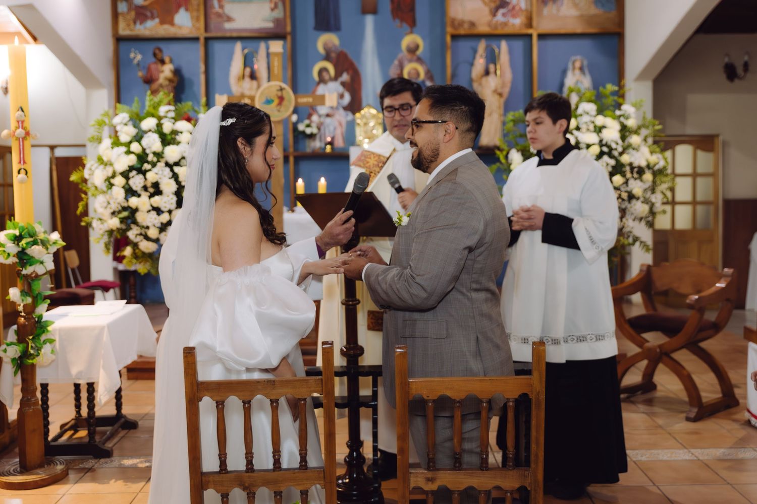 Bride and groom exchange vows at the altar of a decorated Catholic church during their wedding ceremony.
