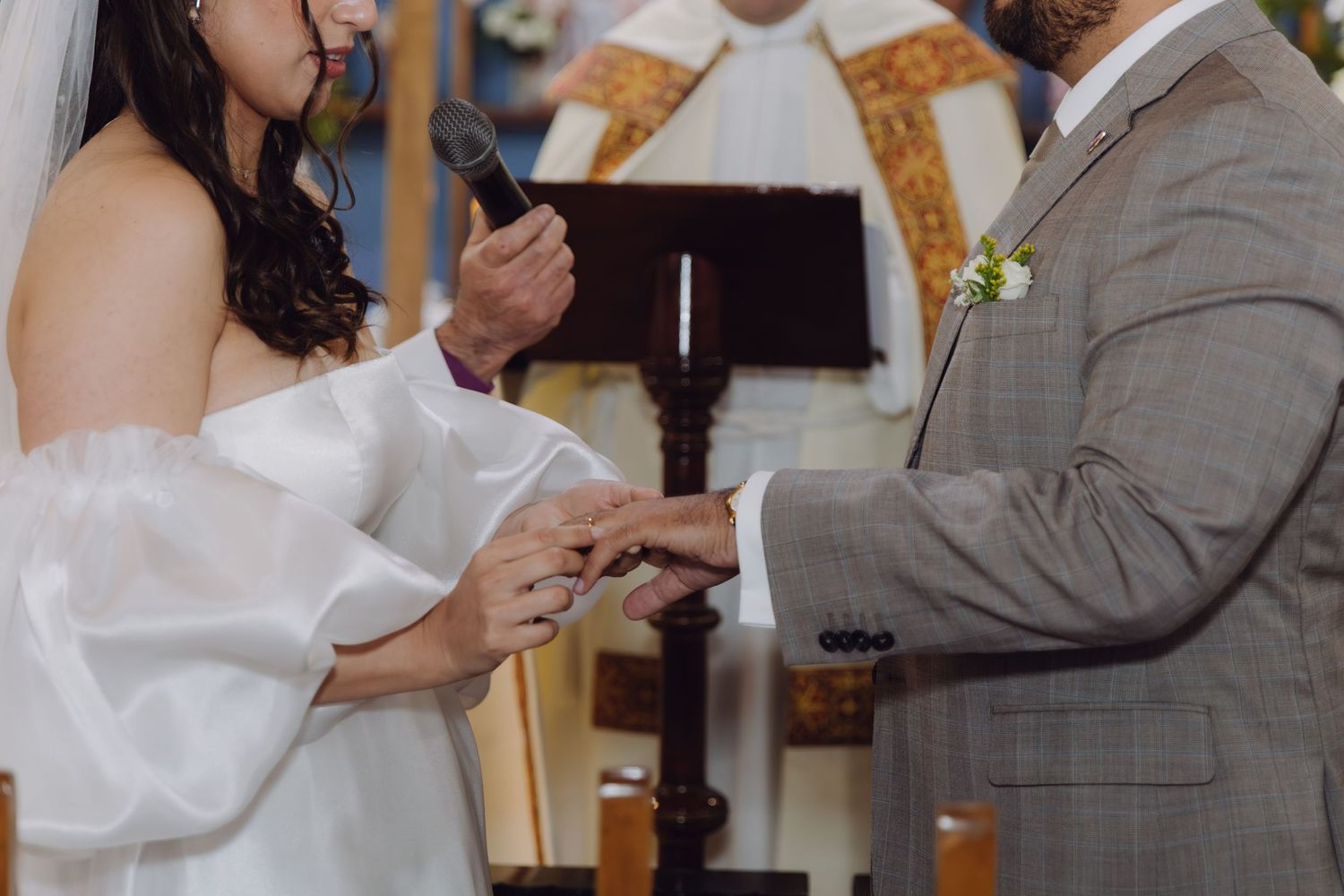 Close-up of a bride placing a wedding ring on the groom's finger during a church ceremony.
