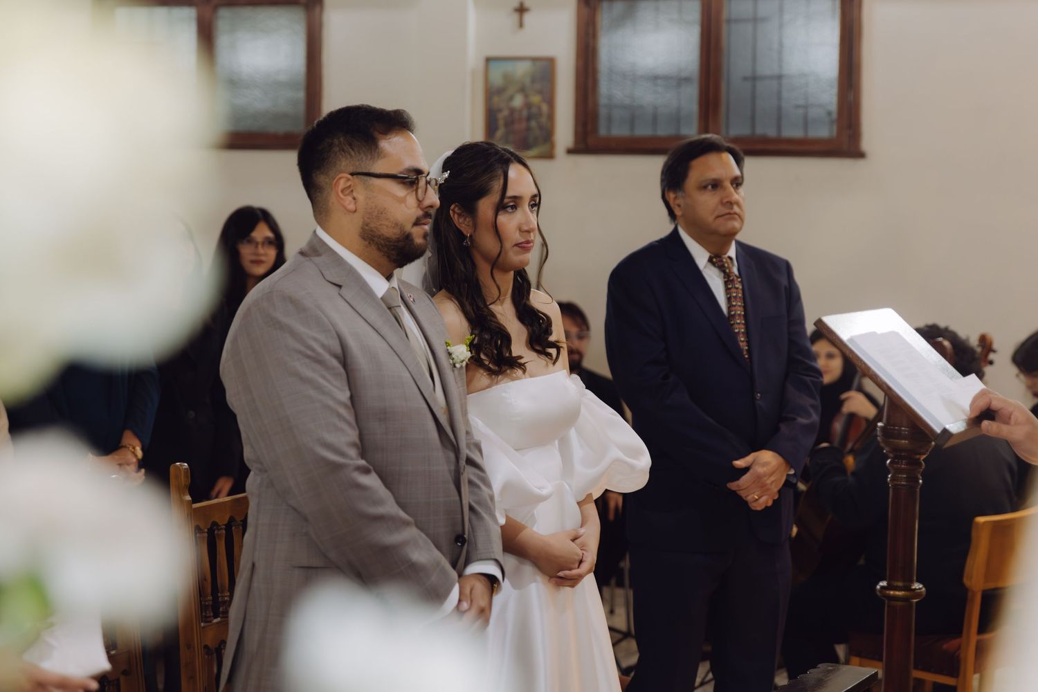 Bride and groom stand together at the church altar during their wedding ceremony with guests in the background.