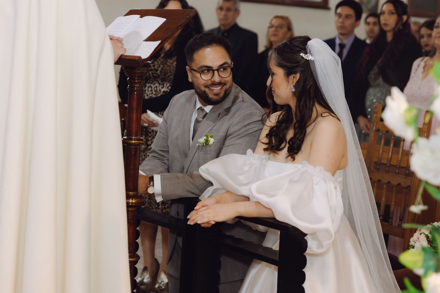 Bride and groom smile at each other while seated at the church altar during their wedding ceremony.