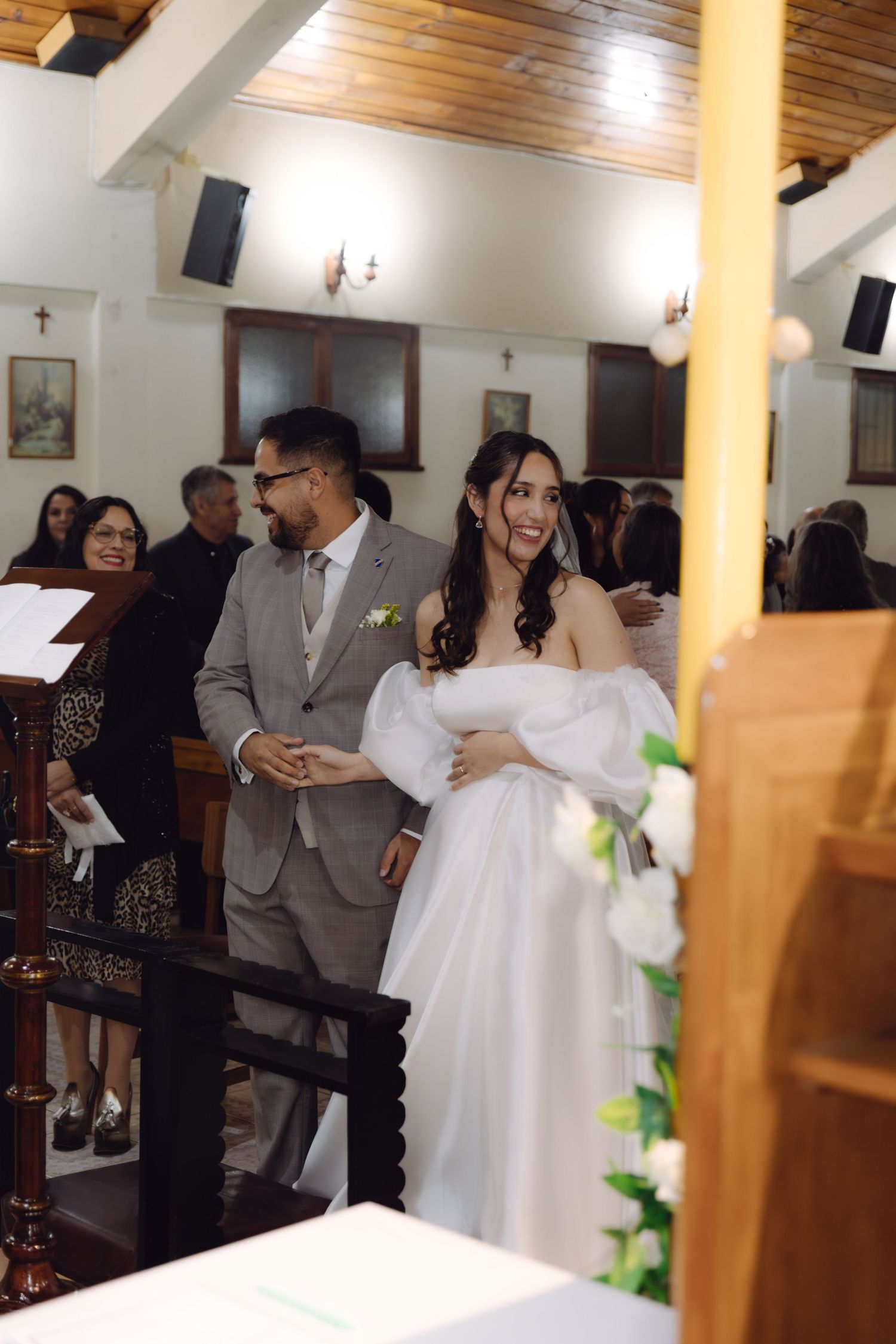 Bride laughs joyfully while holding the groom's hand during their church wedding ceremony with guests behind them.