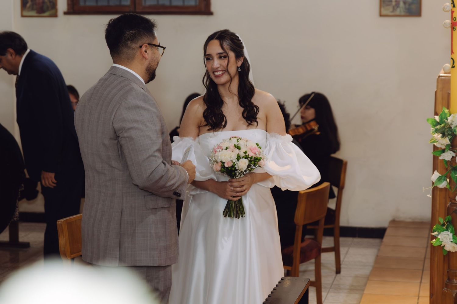 Radiant bride in white puff-sleeve dress holds bouquet while facing groom during church wedding ceremony.