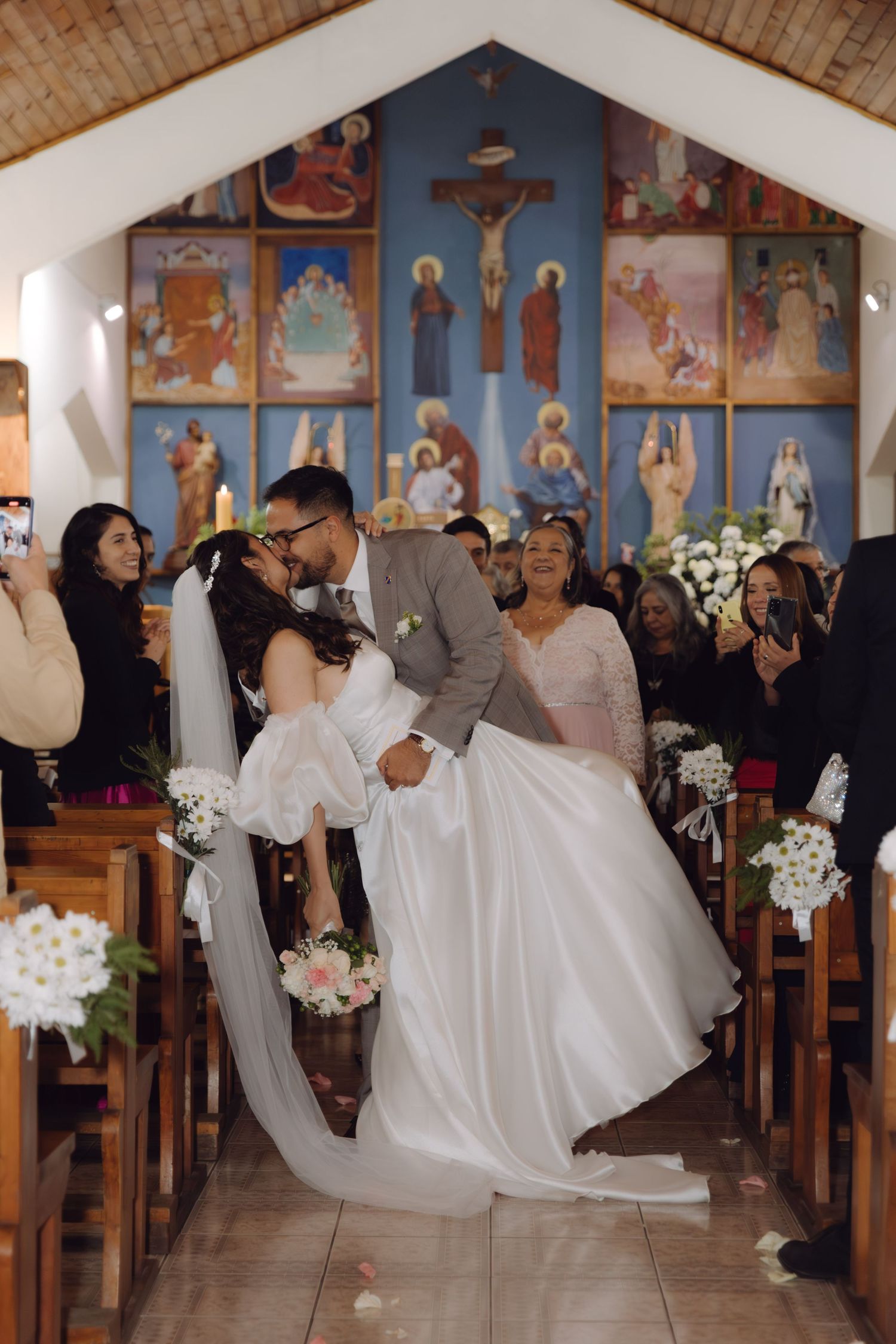 Groom dips bride for romantic kiss in church aisle after wedding ceremony with guests applauding.