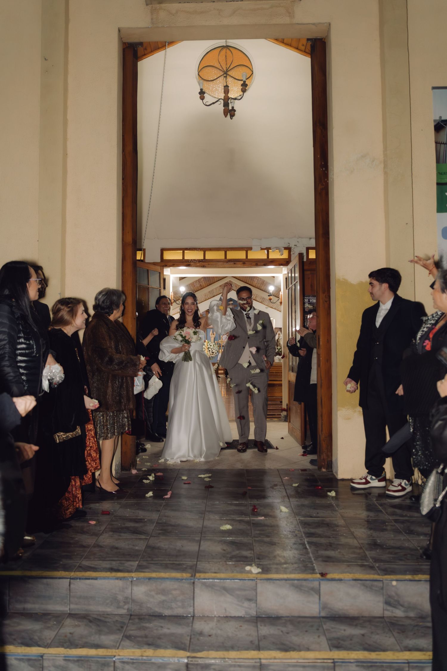 Newlywed couple exits church through grand doorway as guests line up to celebrate their marriage.