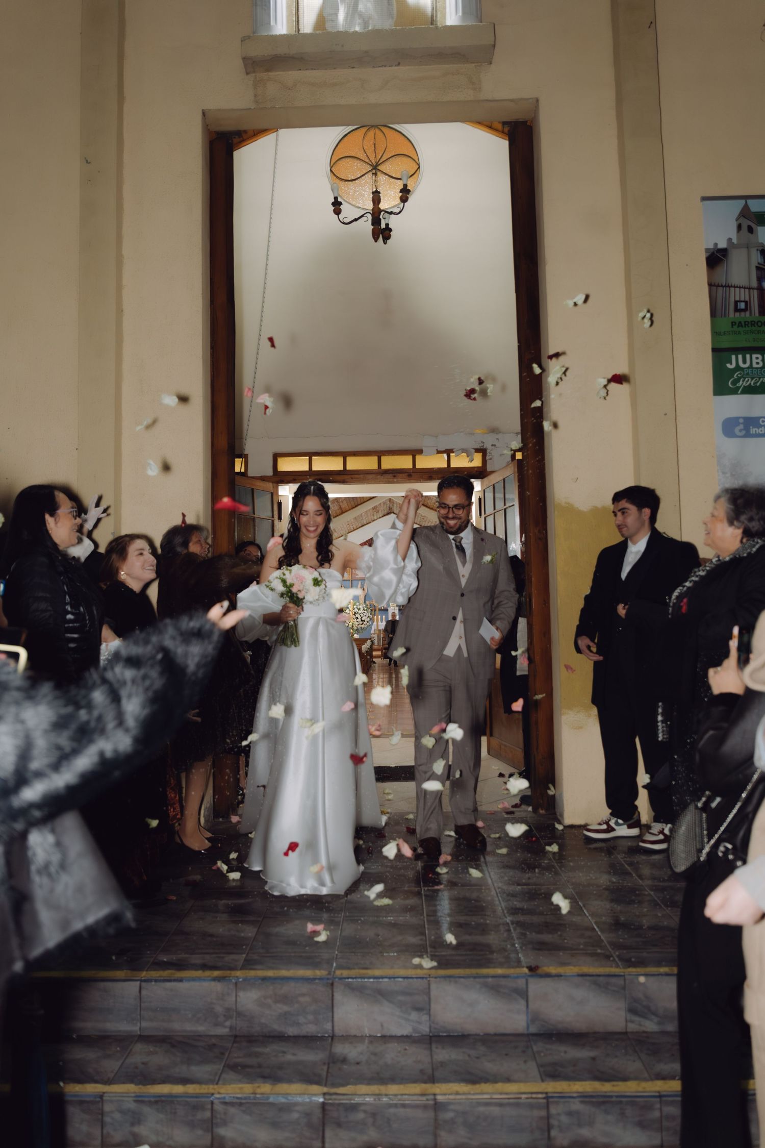 Newlyweds exit church entrance as guests toss flower petals in joyful wedding celebration.
