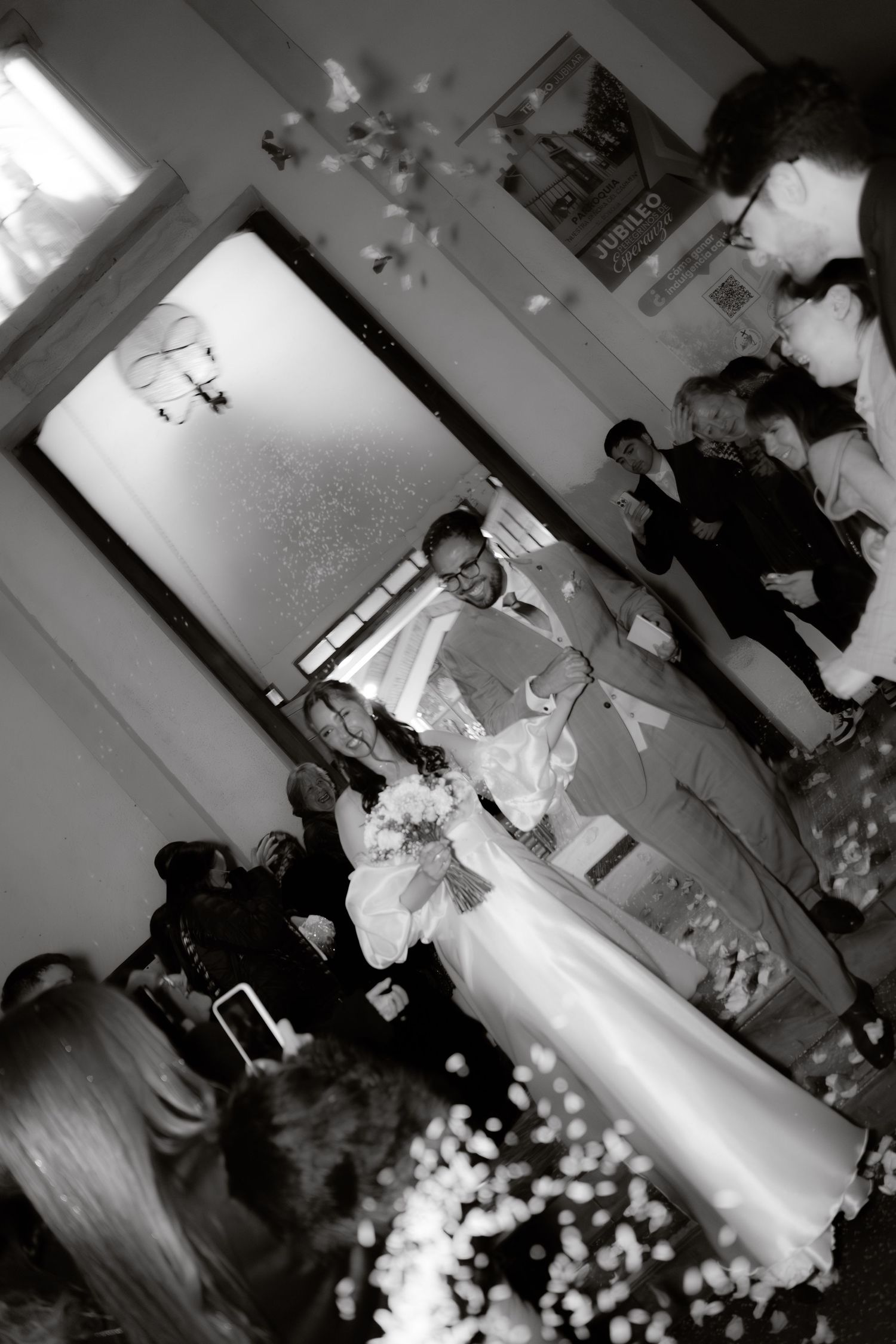 Black and white photo of bride and groom exiting wedding venue amid confetti shower.