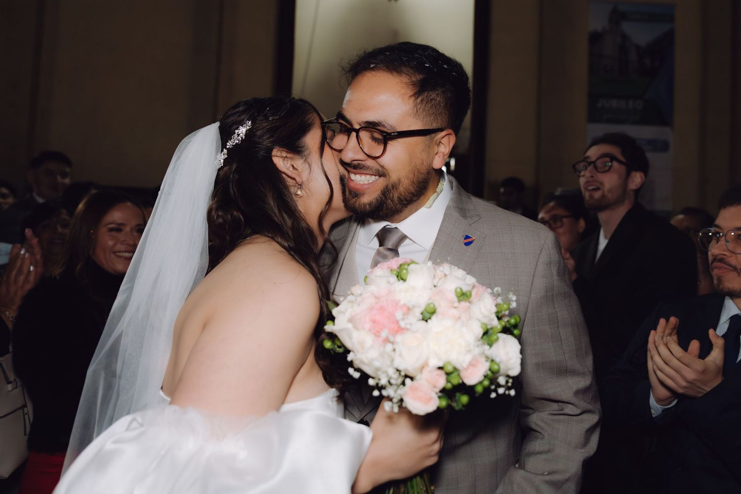 Bride and groom share a romantic kiss while holding a pink and white wedding bouquet.