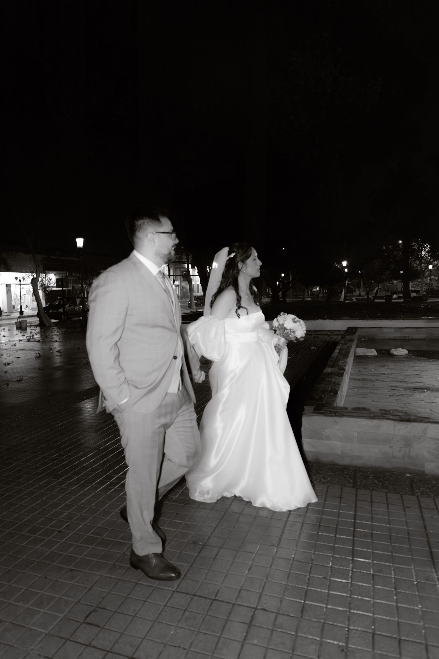 Black and white photo of newlyweds walking together outdoors at night after wedding.