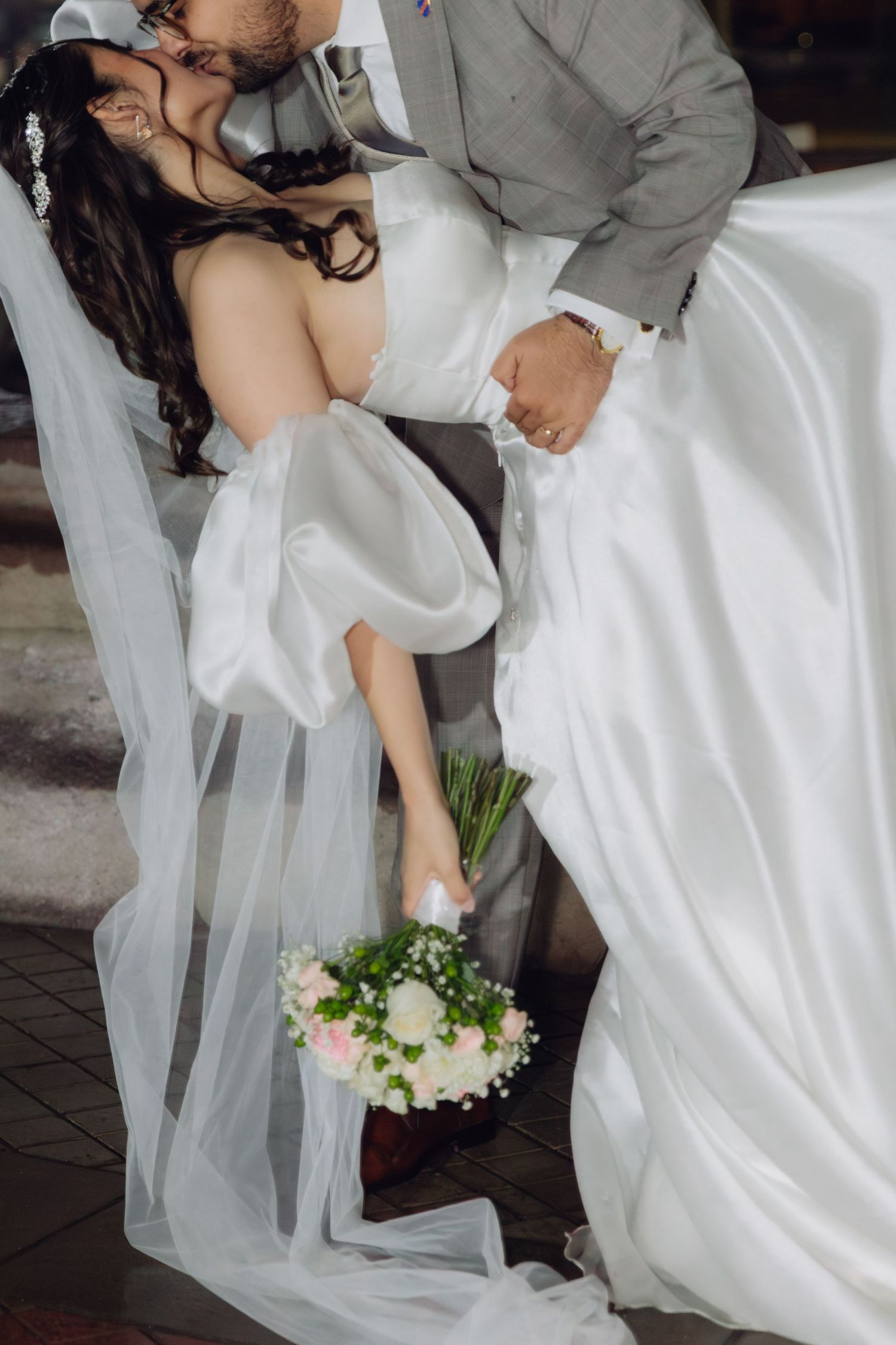 Close-up of groom dipping bride in a white gown while she holds a pink and white bouquet.