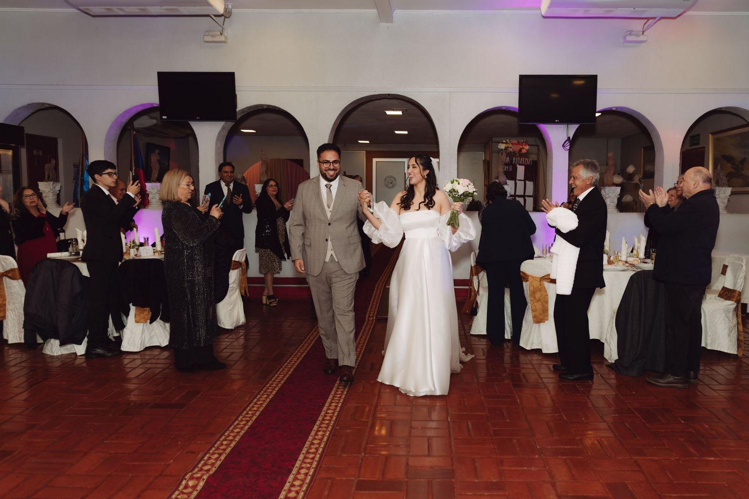 Bride and groom make a grand entrance into their wedding reception hall with guests applauding.